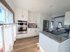 A modern kitchen with white cabinetry, stainless steel appliances, and a marble countertop.