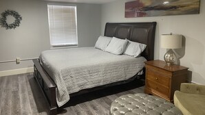 Une chambre à coucher comprenant un lit, une commode, une lampe, une chaise, une fenêtre avec des stores et un élément de décoration murale.