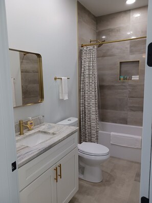 A modern bathroom with a marble vanity, a toilet, and a shower with a patterned curtain. - Tucson Barrio Home 2B/2B (Tucson)