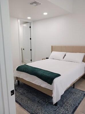 A bedroom with a bed, a nightstand, a bedside table, a wall-mounted shelf, and a door. - Tucson Barrio Home 2B/2B (Tucson)
