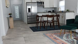 A modern kitchen with white cabinets, stainless steel appliances, and a dining area with wooden chairs.