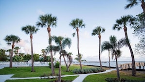 A landscaped area with palm trees, a pathway, and a view of the water. - Caribbean Shores Vacation Rentals (Jensen Beach)