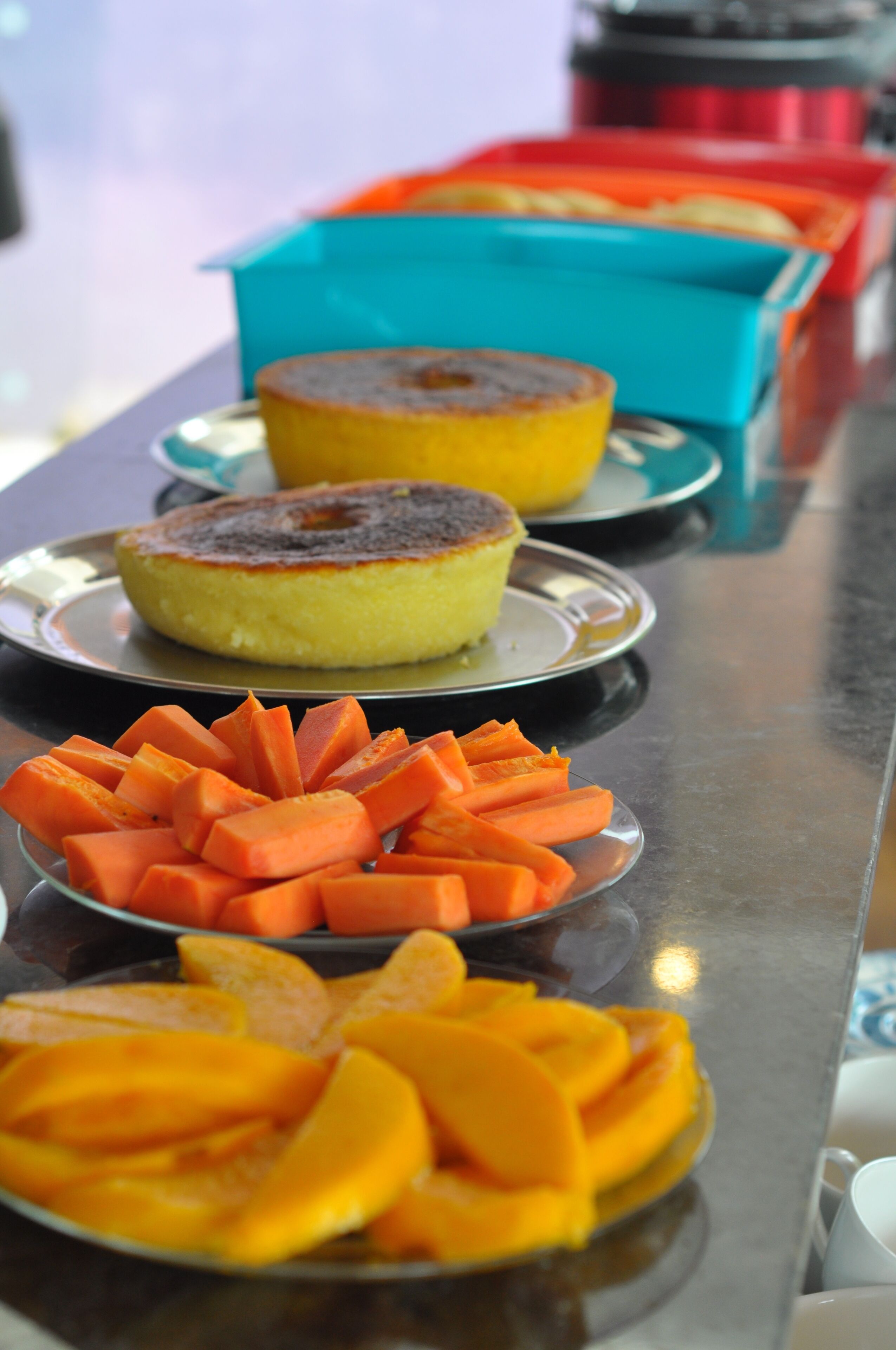 A buffet table with plates of food including a cake, sliced carrots, and mangoes.