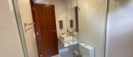A bathroom with a glass shower enclosure, a wooden door, a white toilet, and a sink with a mirror above it.