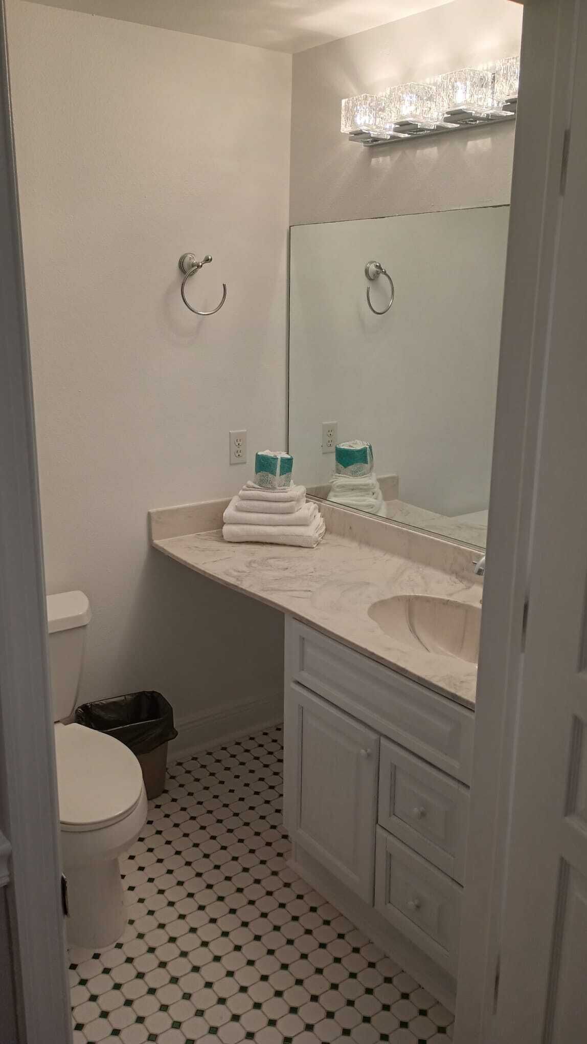 Une salle de bain comprenant des toilettes, un lavabo, un miroir et un sol carrelé.