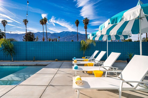 A poolside area with lounge chairs, umbrellas, and a view of mountains. - Stunning mountain views! New midcentury modern gem in the heart of Palm Springs! (Palm Springs)