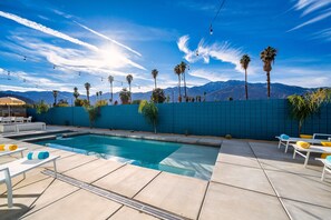 A swimming pool with lounge chairs and a blue wall, surrounded by palm trees and mountains. - Stunning mountain views! New midcentury modern gem in the heart of Palm Springs! (Palm Springs)