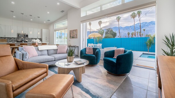 A spacious living area with a modern kitchen, comfortable seating, and a view of a pool and mountains.