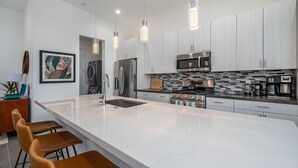 A modern kitchen with a large island, stainless steel appliances, and pendant lighting.