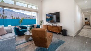A spacious living room with a large TV, comfortable seating, and a view of mountains through large windows.