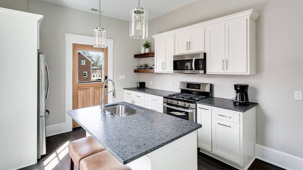 A modern kitchen with white cabinets, a granite countertop, stainless steel appliances, and pendant lighting.