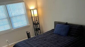 Un dormitorio con cama, mesita de noche, lámpara y ventana con persianas.