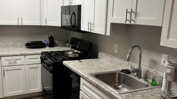 Una cocina moderna con gabinetes blancos, un fregadero de acero inoxidable, una estufa y un microondas.