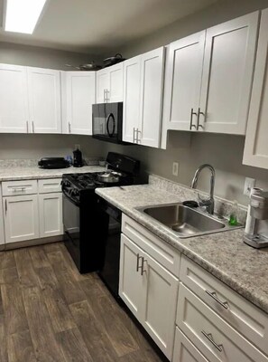 A modern kitchen with white cabinets, a stainless steel sink, a stove, and a microwave. - Fun Friendly 2 bedroom. (Greensboro)