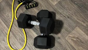 Un par de mancuernas negras con mangos amarillos sobre un piso de madera.