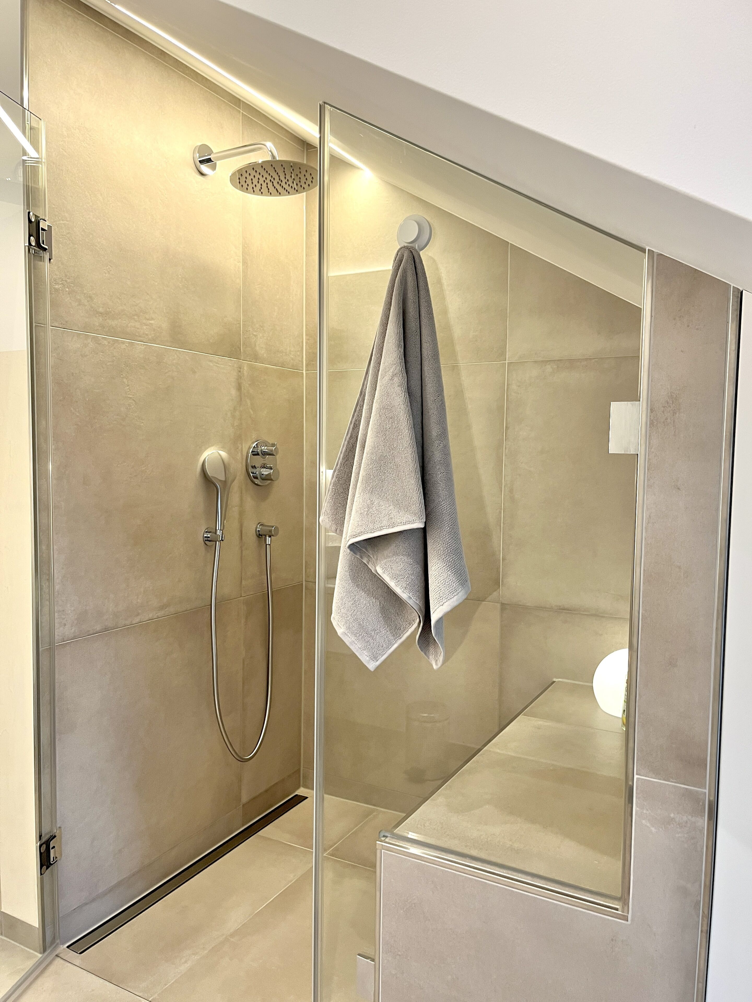 A modern bathroom with a glass-enclosed shower, a towel rack, and a visible showerhead.