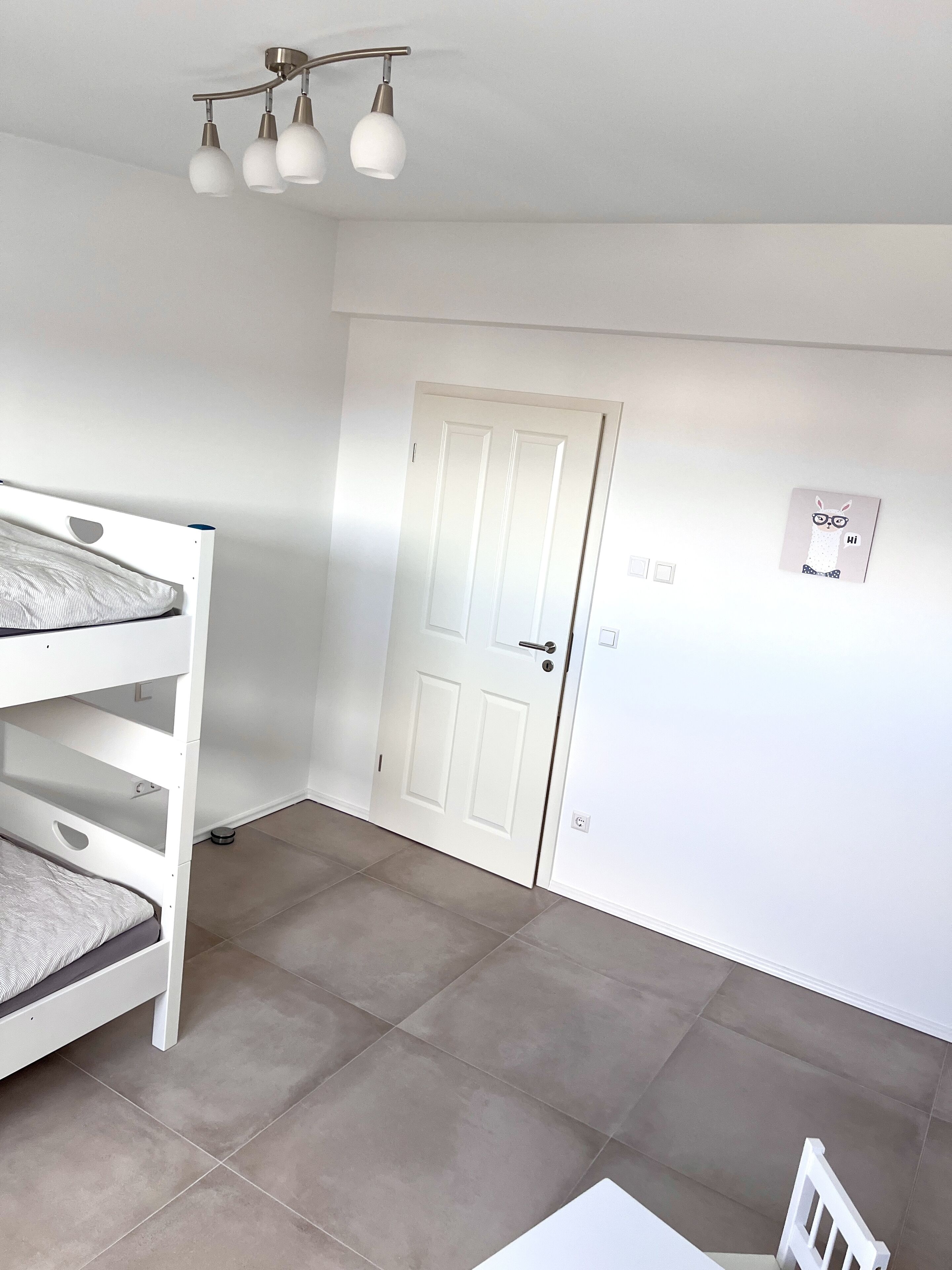 Una habitación con literas, una puerta blanca y una lámpara en el techo.