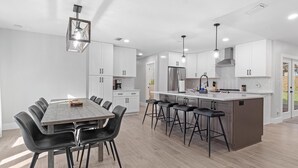 A modern kitchen with white cabinets, a central island with bar stools, and pendant lighting. - Airy, Spacious, Newly Renovated Home – Walk to UF! (Gainesville)