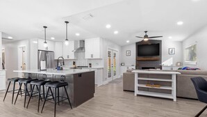 A modern kitchen with white cabinets, a central island with stools, a built-in oven, and a ceiling fan. - Airy, Spacious, Newly Renovated Home – Walk to UF! (Gainesville)