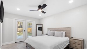 A bedroom with a bed, bedside table, nightstand, ceiling fan, and a TV mounted on the wall. - Airy, Spacious, Newly Renovated Home – Walk to UF! (Gainesville)