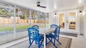 A covered patio with a table and chairs, large windows, and a ceiling fan. - Airy, Spacious, Newly Renovated Home – Walk to UF! (Gainesville)