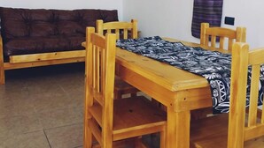 A dining area with a wooden table and chairs, a brown sofa, and a patterned curtain. - RUKA Apart  (Chilecito)