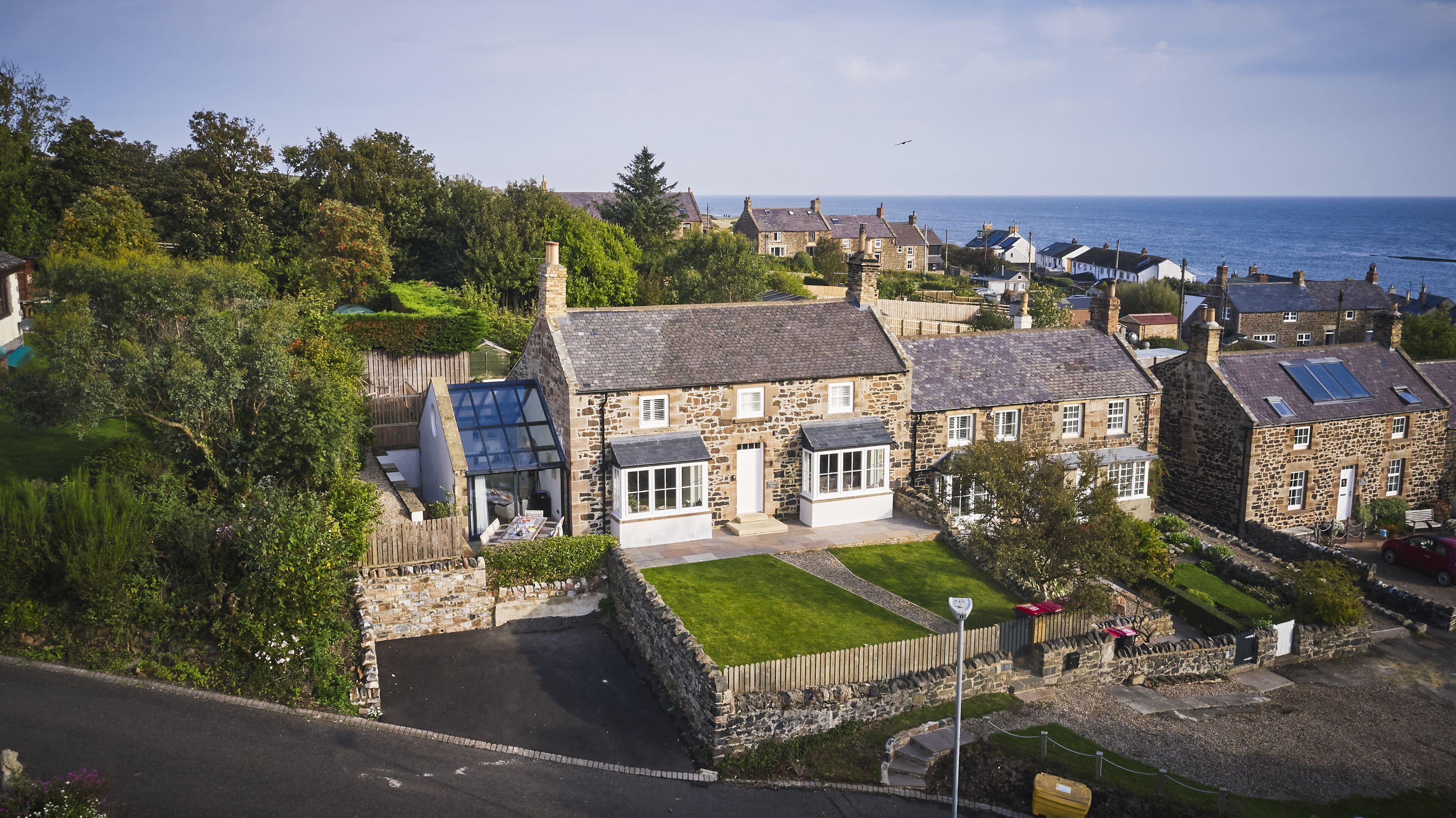 A coastal village with stone houses, a grassy lawn, and a view of the sea.