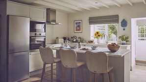 A kitchen with a central island, bar stools, a refrigerator, and a clock on the wall. - Driftwood -  a pet friendly that sleeps 4 guests  in 2 bedrooms (Craster, Alnwick)