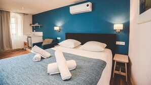 Et hotelværelse med en stor seng, et natbord, et skrivebord med stol, et vindue med gardiner og en aircondition-enhed på væggen.