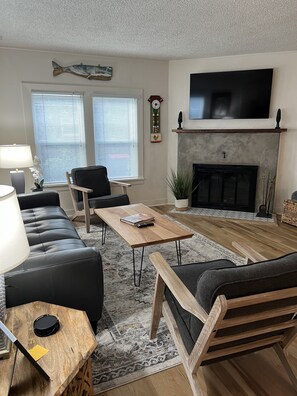 Ein Wohnzimmer mit Sofa, Sesseln, Couchtisch, Kamin, Fernseher und einer Uhr.