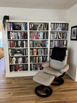 Ein Zimmer mit einer großen Bücherwand, einem Ledersessel und einem Holzboden.