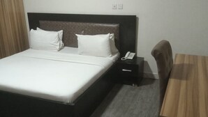 A hotel room with a bed, bedside table, and a desk. - Sky Suites (Lagos)