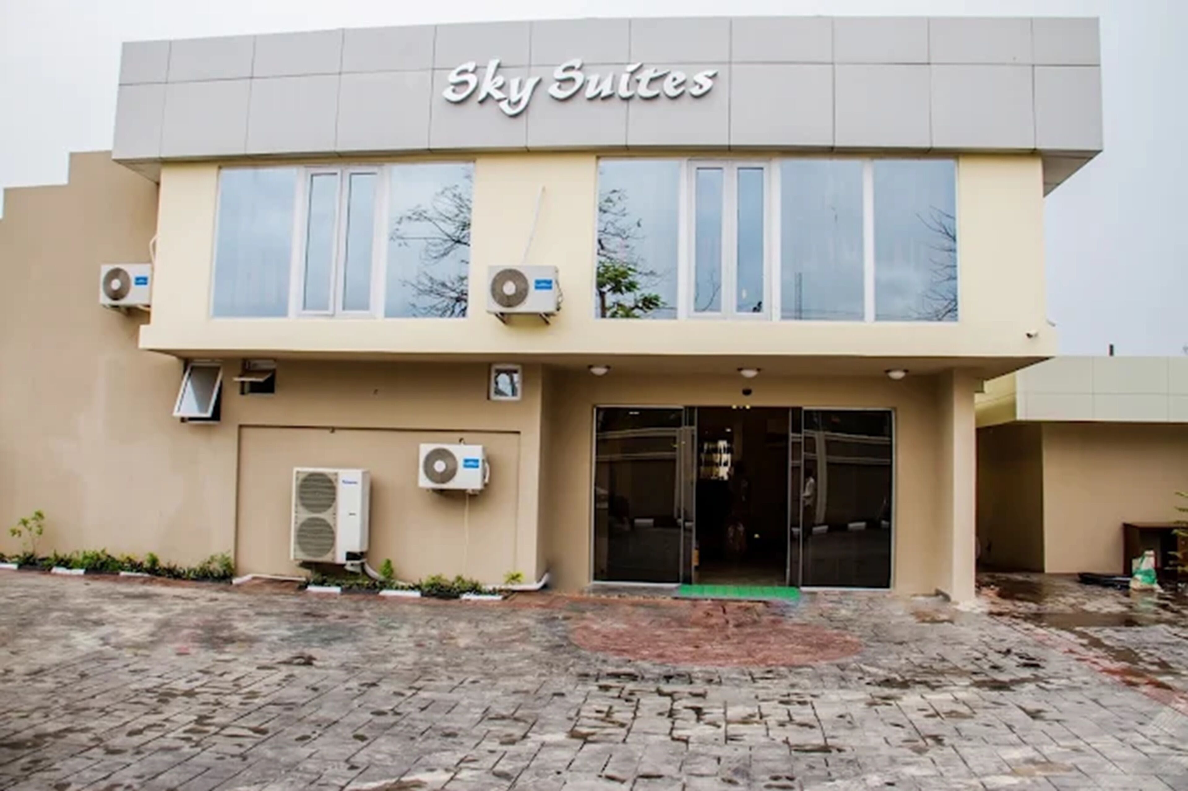 Un edificio con el letrero 'Sky Suites' sobre la entrada. Se observan unidades de aire acondicionado instaladas en las paredes exteriores.