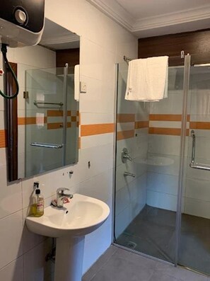 Une salle de bain avec une douche à parois de verre, un lavabo avec un miroir et une serviette accrochée à la porte de la douche.