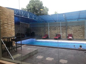 An outdoor swimming pool with red lounge chairs and a brick wall. - Sky Suites (Lagos)
