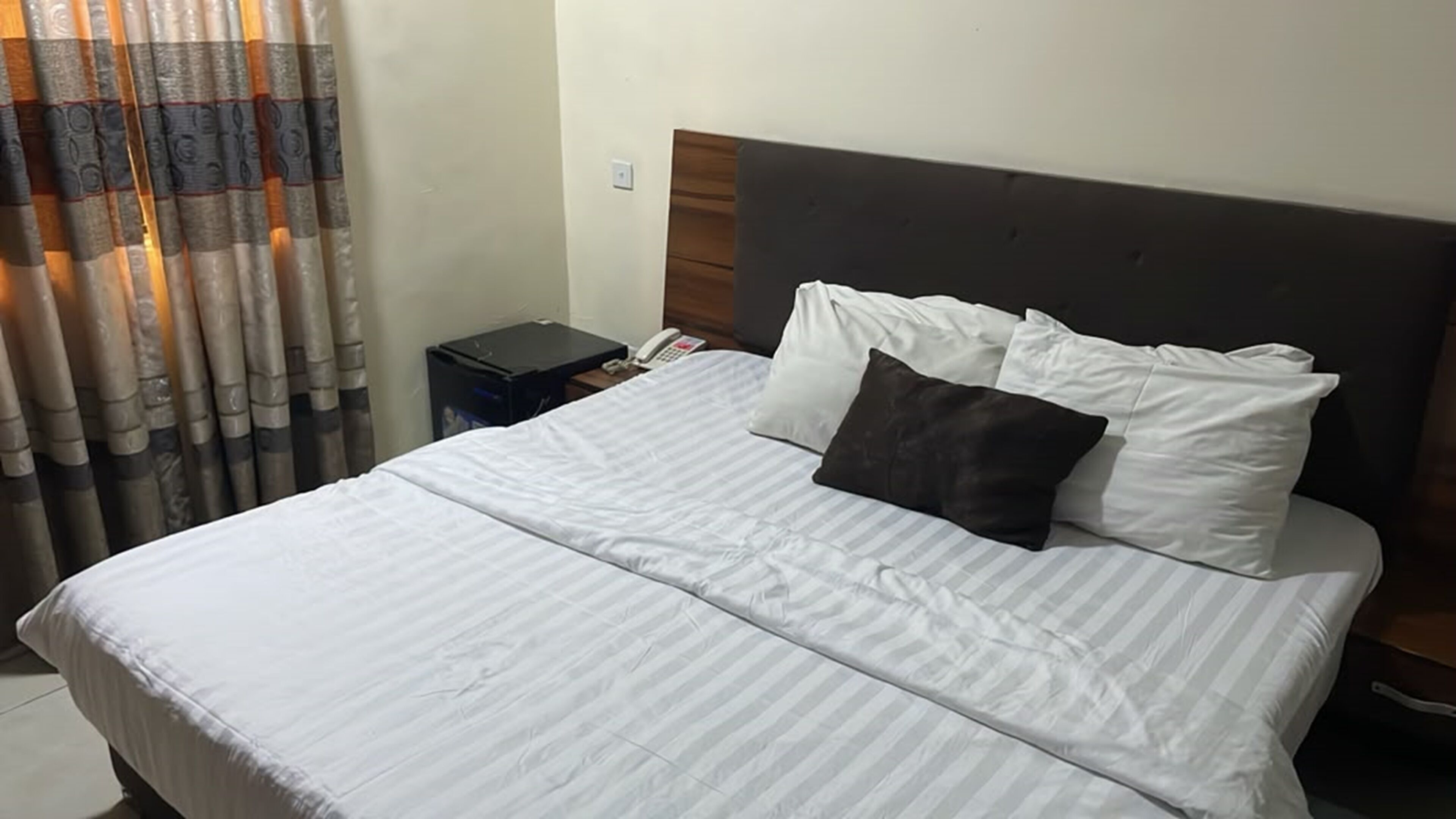 A hotel room with a bed, a nightstand, a telephone, and a curtain.