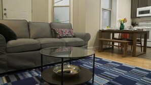 Ein Wohnzimmer mit einer Couch, einem Glastisch und einem gemusterten Teppich.
