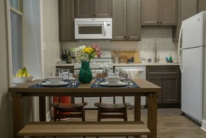 Una cocina con armarios de madera, un microondas blanco y una mesa de comedor dispuesta con platos, vasos y un jarrón de flores.