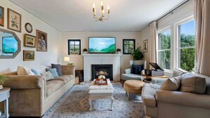 A living room with a fireplace, sofas, a coffee table, and a TV. - Charming cottage in the city; walk to Main Street (Vancouver)