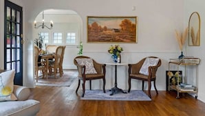 A dining area with two wooden chairs, a round table, and a painting on the wall. - Charming cottage in the city; walk to Main Street (Vancouver)