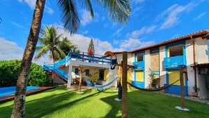 A two-story building with a blue and white exterior, a swimming pool, and a hammock in the yard. - Manaí Pousada & Beach Club (Barra de Santo Antonio)