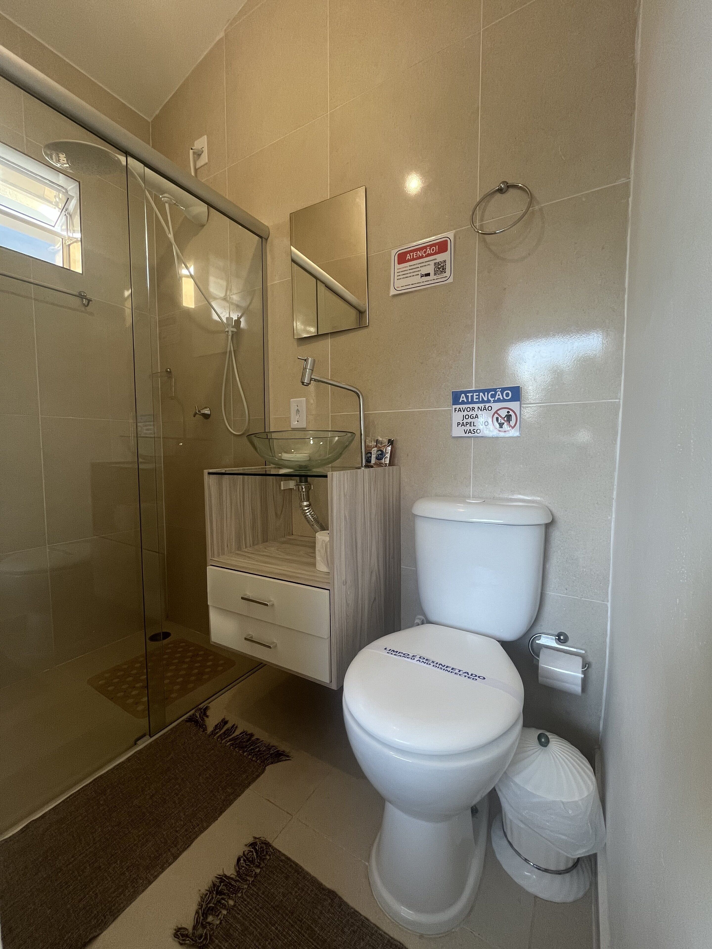 A modern bathroom with a glass-enclosed shower, a white sink with a marble countertop, and a toilet with a lid that has text on it.