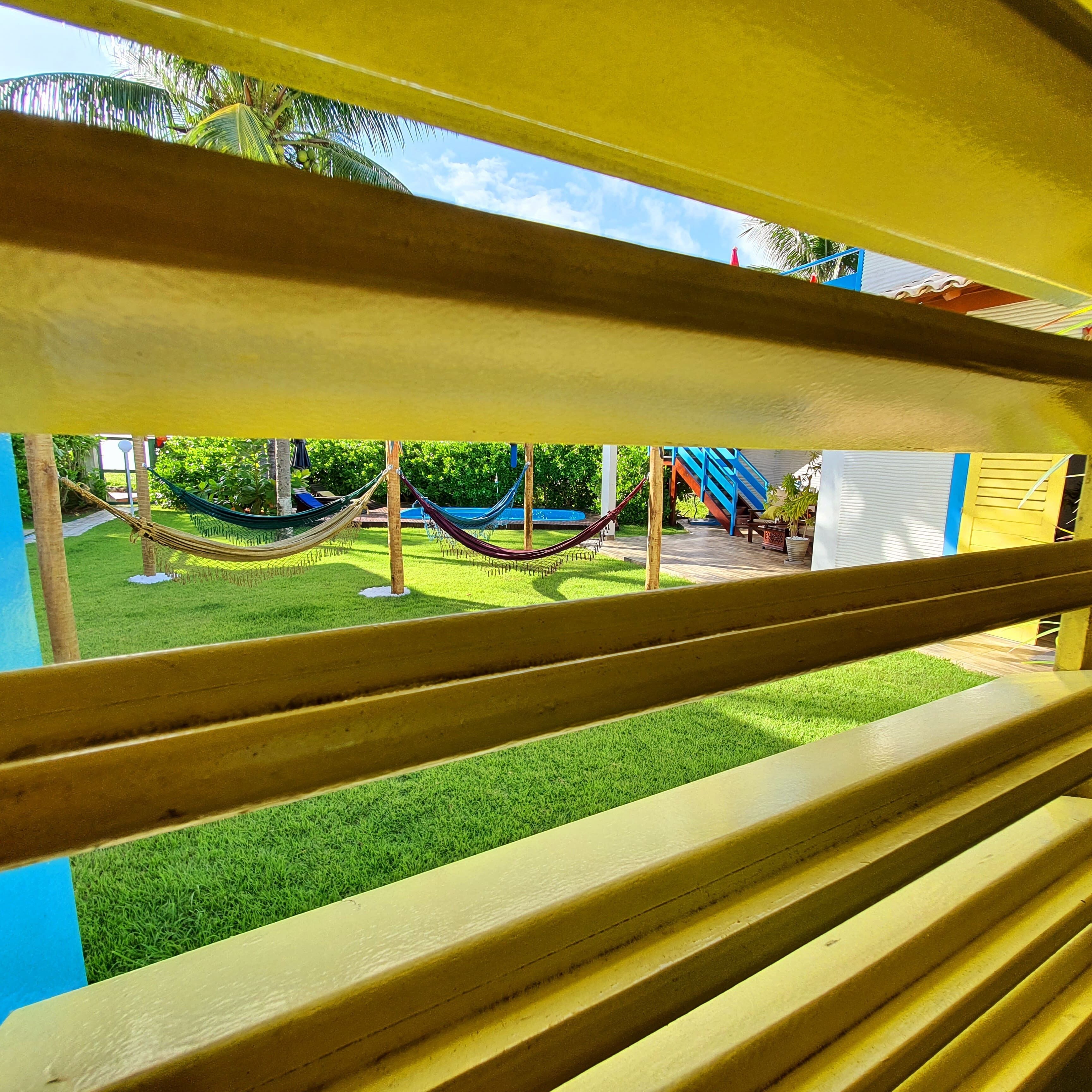 Vista a través de una ventana con marco de madera, que da a una zona cubierta de césped con una hamaca y un parque infantil.