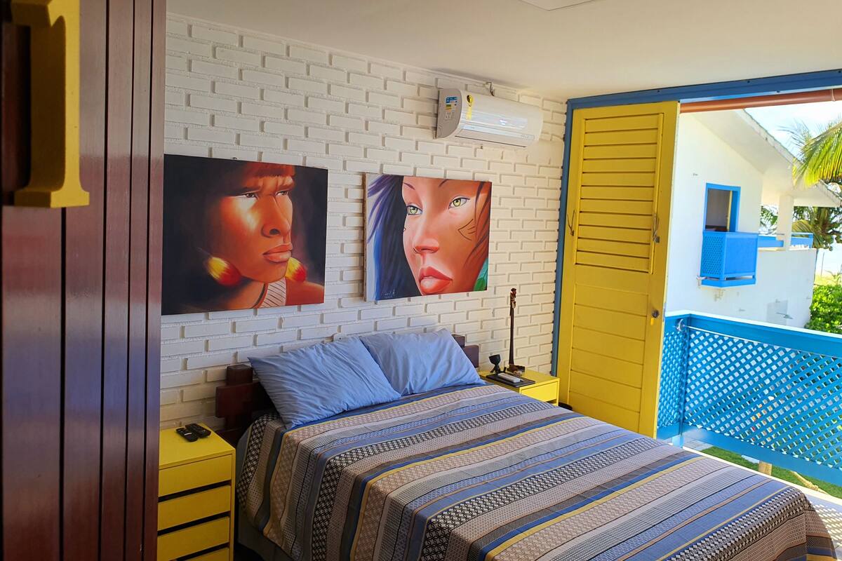 A bedroom with a bed, a nightstand, a wall-mounted air conditioner, and two paintings.