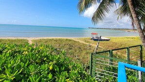 A beach view with a boat, palm trees, and a fence. - Manaí Pousada & Beach Club (Barra de Santo Antonio)