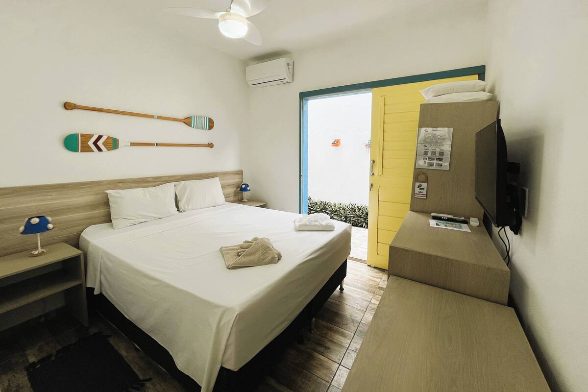 A hotel room with a bed, a desk, a television, a ceiling fan, and a door leading to a balcony.