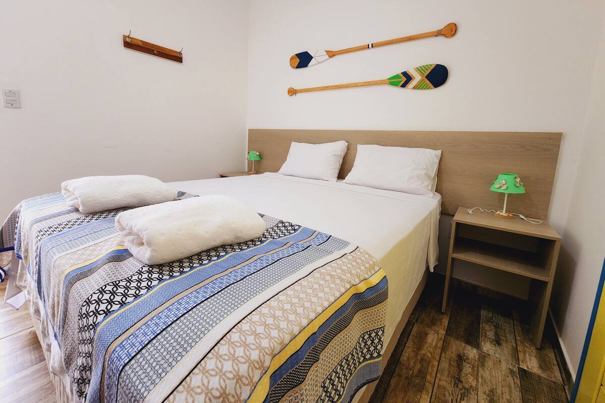 A neatly made bed with patterned bedding, two pillows, a bedside lamp, and two wooden paddles on the wall.