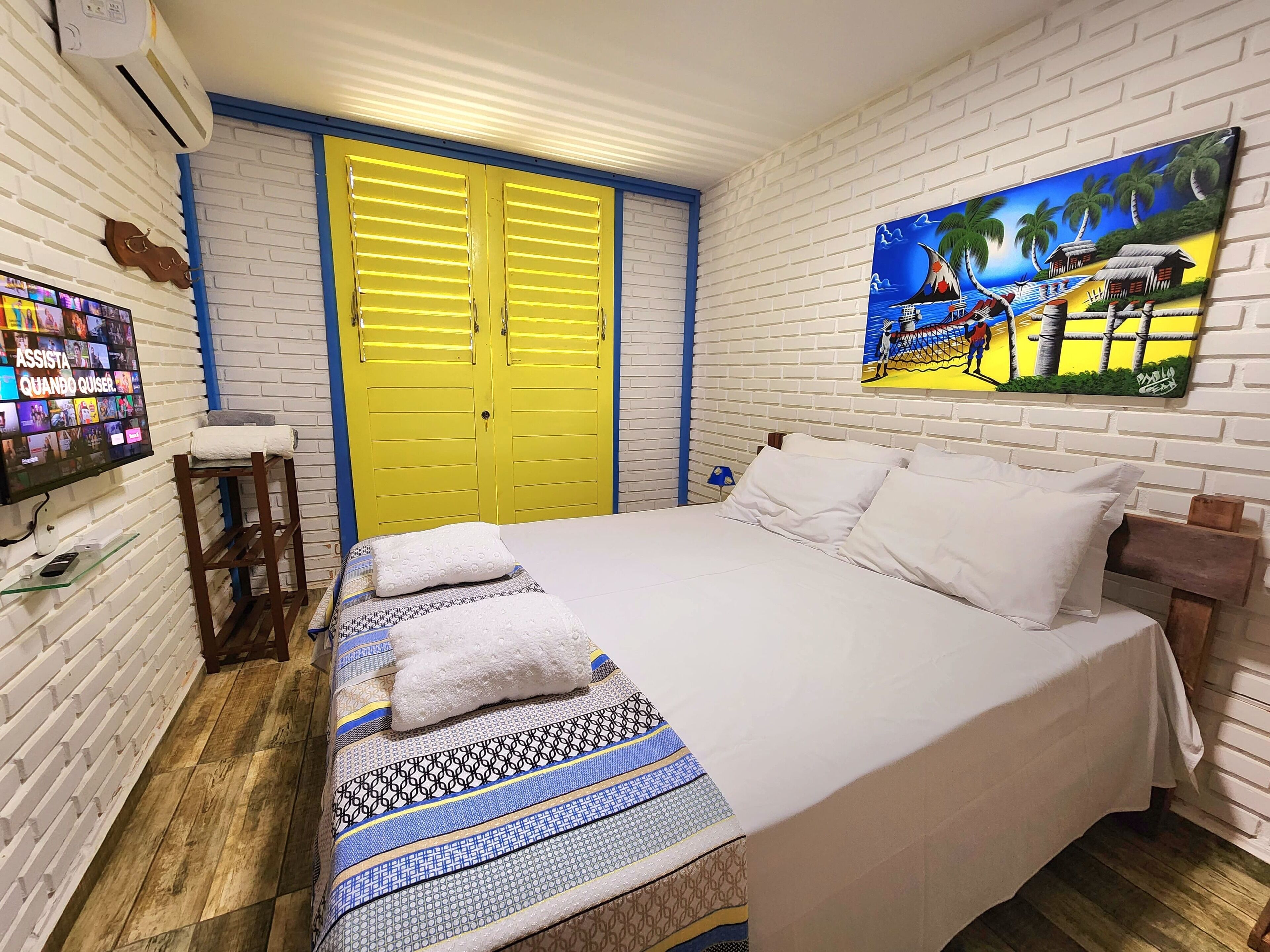 A bedroom with a bed, a TV, a yellow door, and a painting.