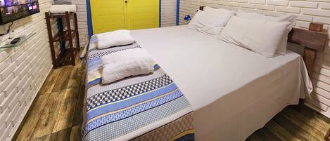 A bedroom with a bed, a TV, a yellow door, and a painting.