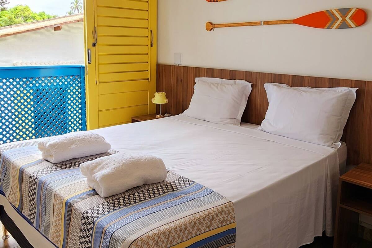 A hotel room with a bed, two pillows, a wooden headboard, a yellow door, and two wooden paddles on the wall.